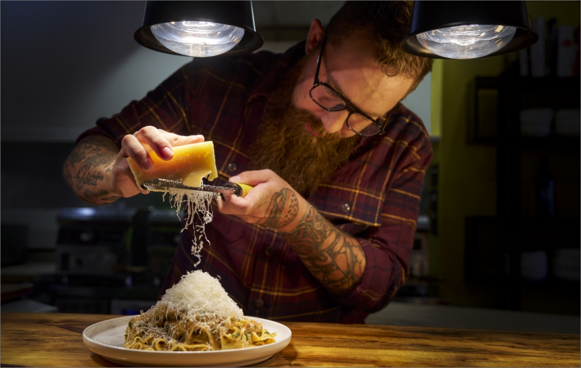 Image of Chef Adam Pawlak grating parmesean cheese over one of his pasta dishes.
