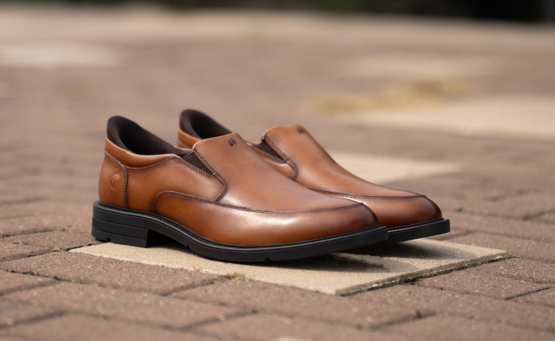 Shop Nunn Bush dress featuring the KORE Icon slip on in cognac on a brick background.